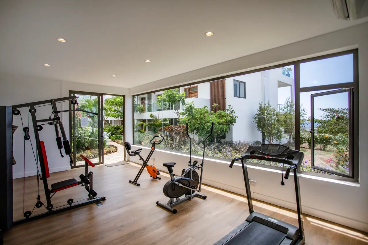 Salle de sport lumineuse, offrant une vue sur la mer et l'extérieur. Équipements variés pour l'entraînement.