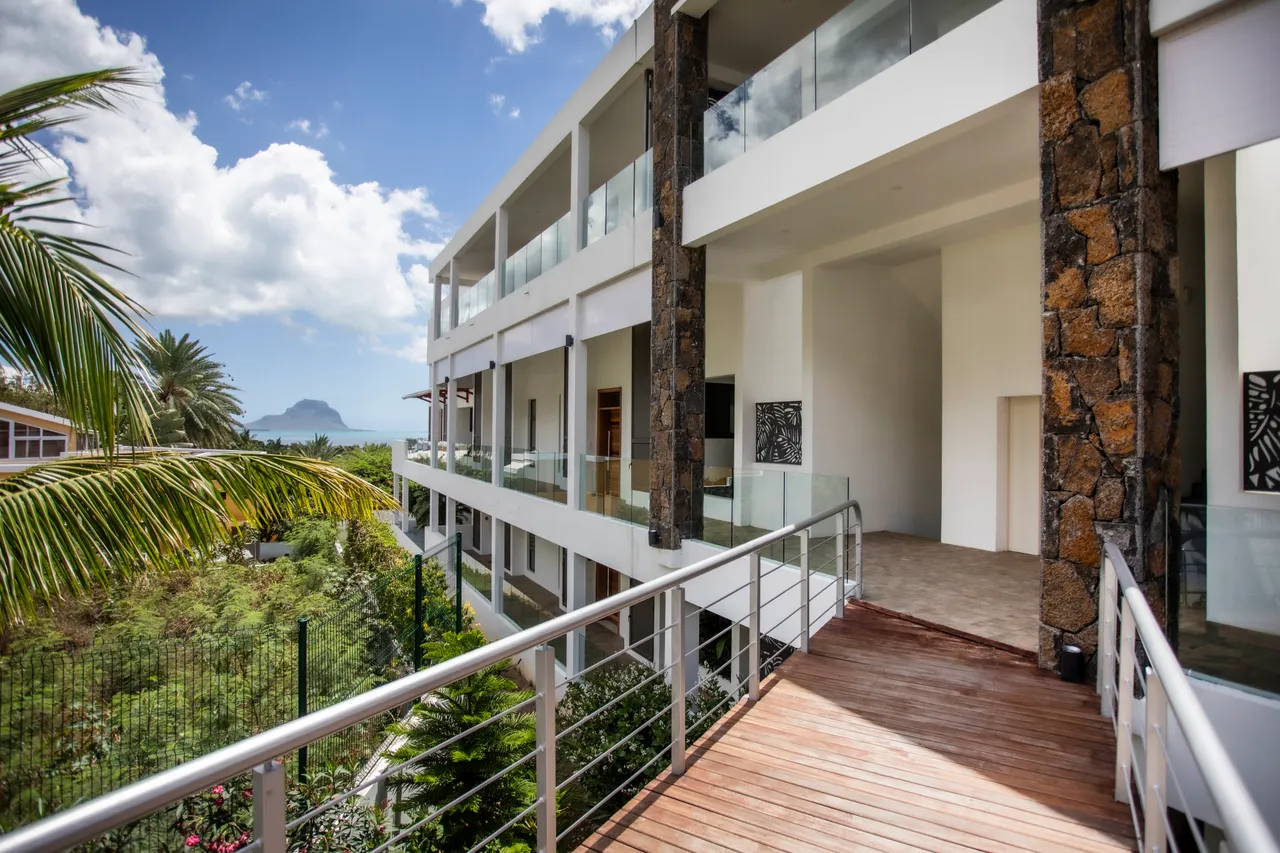Terrasse avec balustrade en métal, vue dégagée sur la mer. Éléments paysagers en arrière-plan.