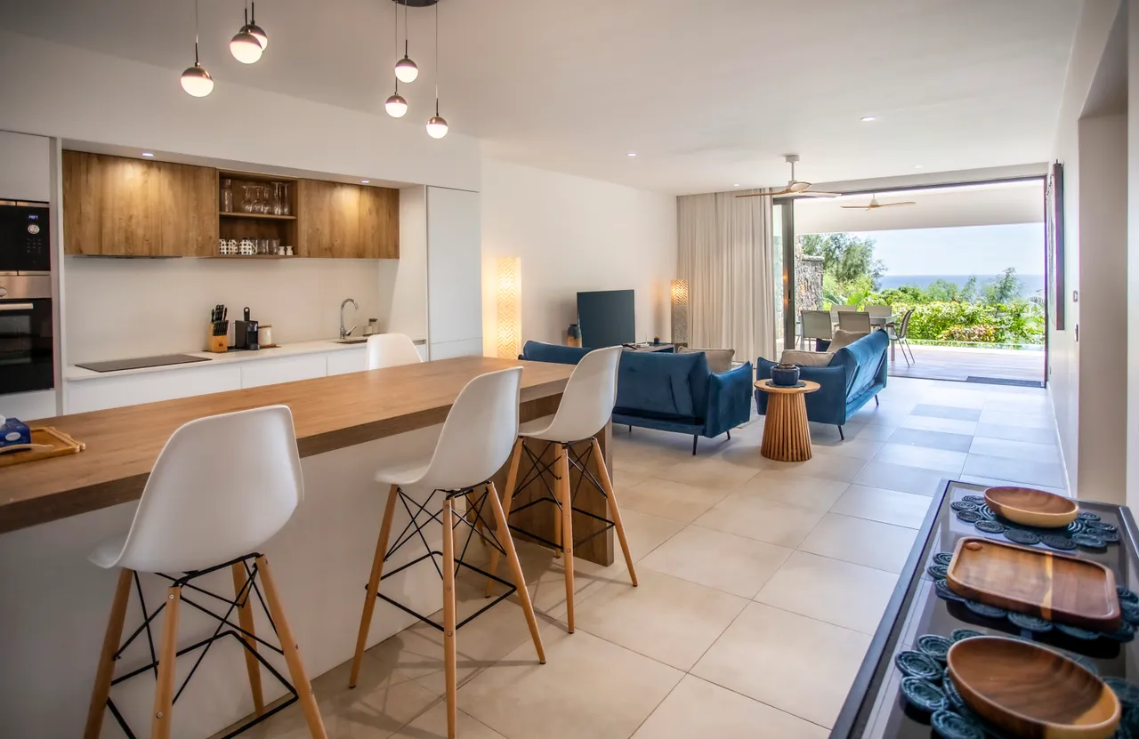 Cuisine ouverte avec bar en bois et chaises hautes. Vue sur la mer.