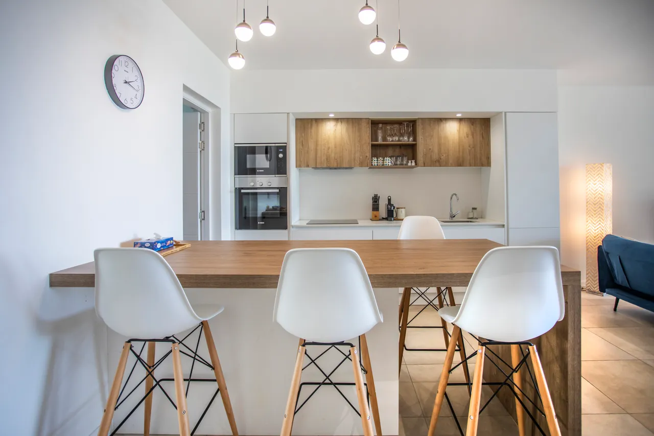 Espace repas lumineux avec bar en bois et chaises blanches. Éclairage moderne.