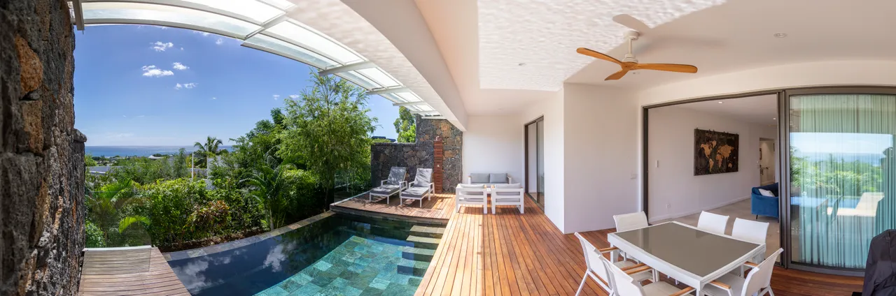 Terrasse en bois avec salon extérieur, vue sur la piscine et la mer. Ambiance fraîche et relaxante.