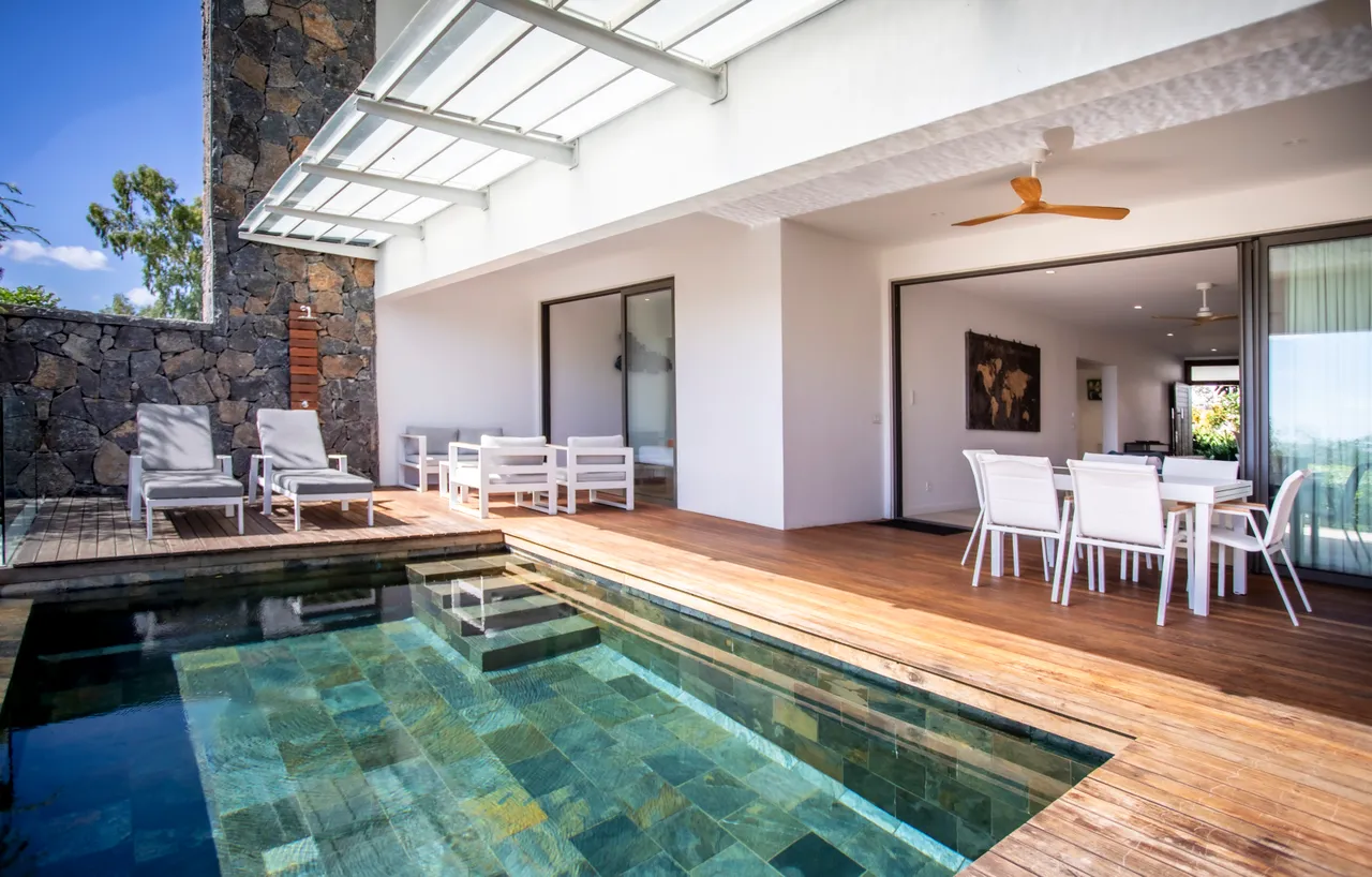 Espace de détente adjacent à la piscine, avec chaises longues et vue mer. Terrasse en bois.