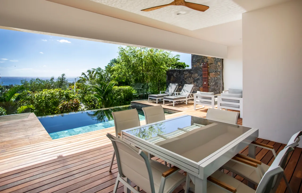 Terrasse en bois avec table à manger, offrant une vue sur la mer. Piscine à débordement à proximité.