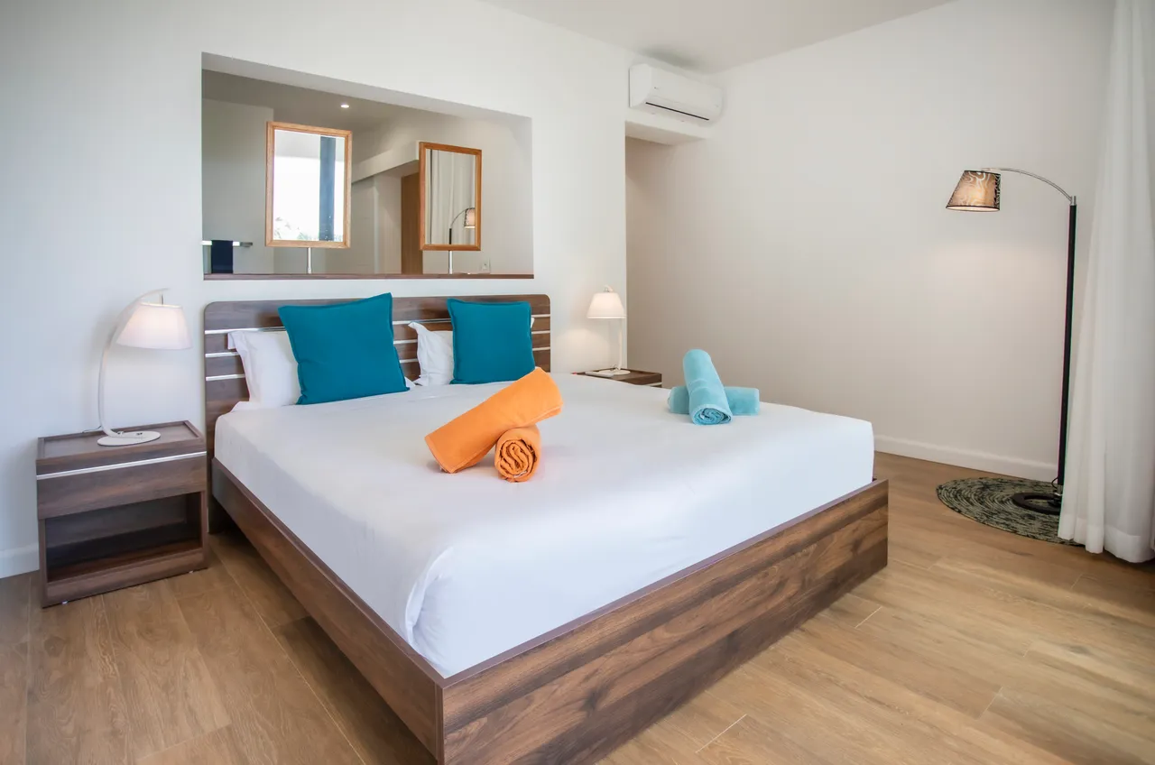 Chambre avec parquet clair et literie blanche. Éclairage doux et vue sur l'extérieur.