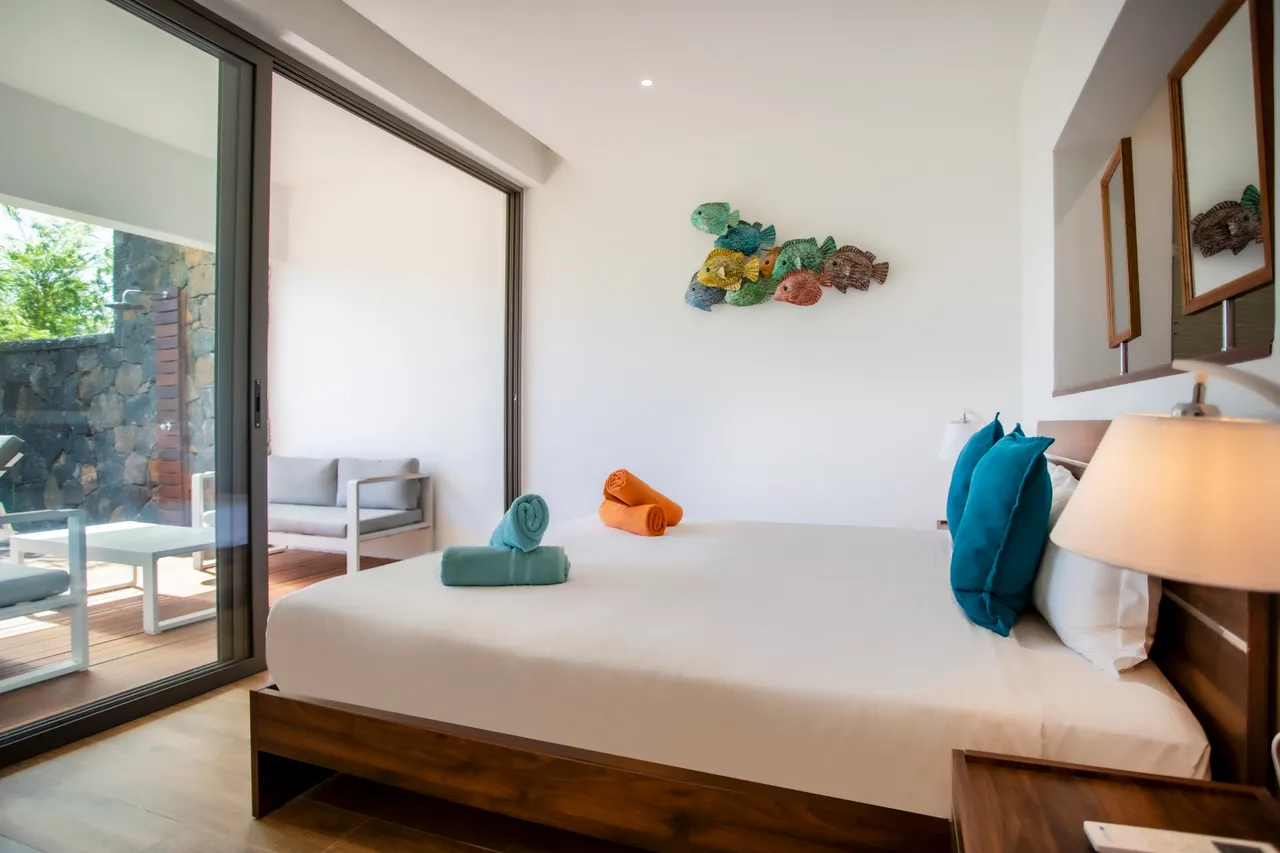 Chambre avec lit double, décorée de coussins colorés. Accès à une terrasse.
