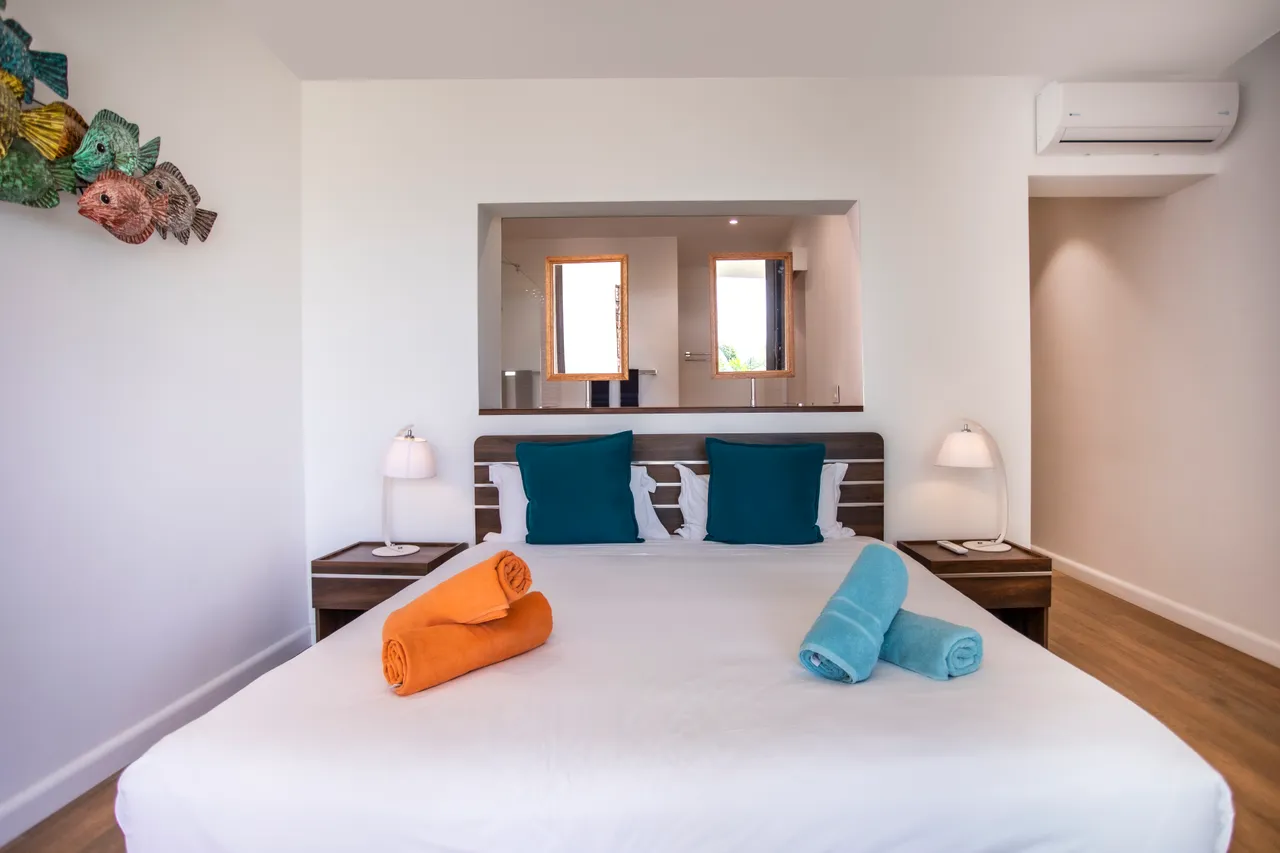 Tons clairs et mobilier minimaliste. Chambre spacieuse avec literie colorée et décoration marine.
