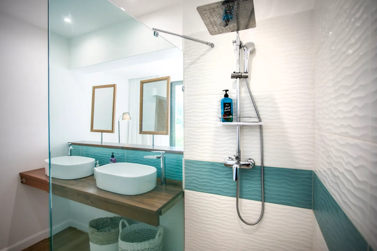 Salle de bain moderne avec douche à l'italienne et deux vasques. Éclairage naturel grâce aux fenêtres.