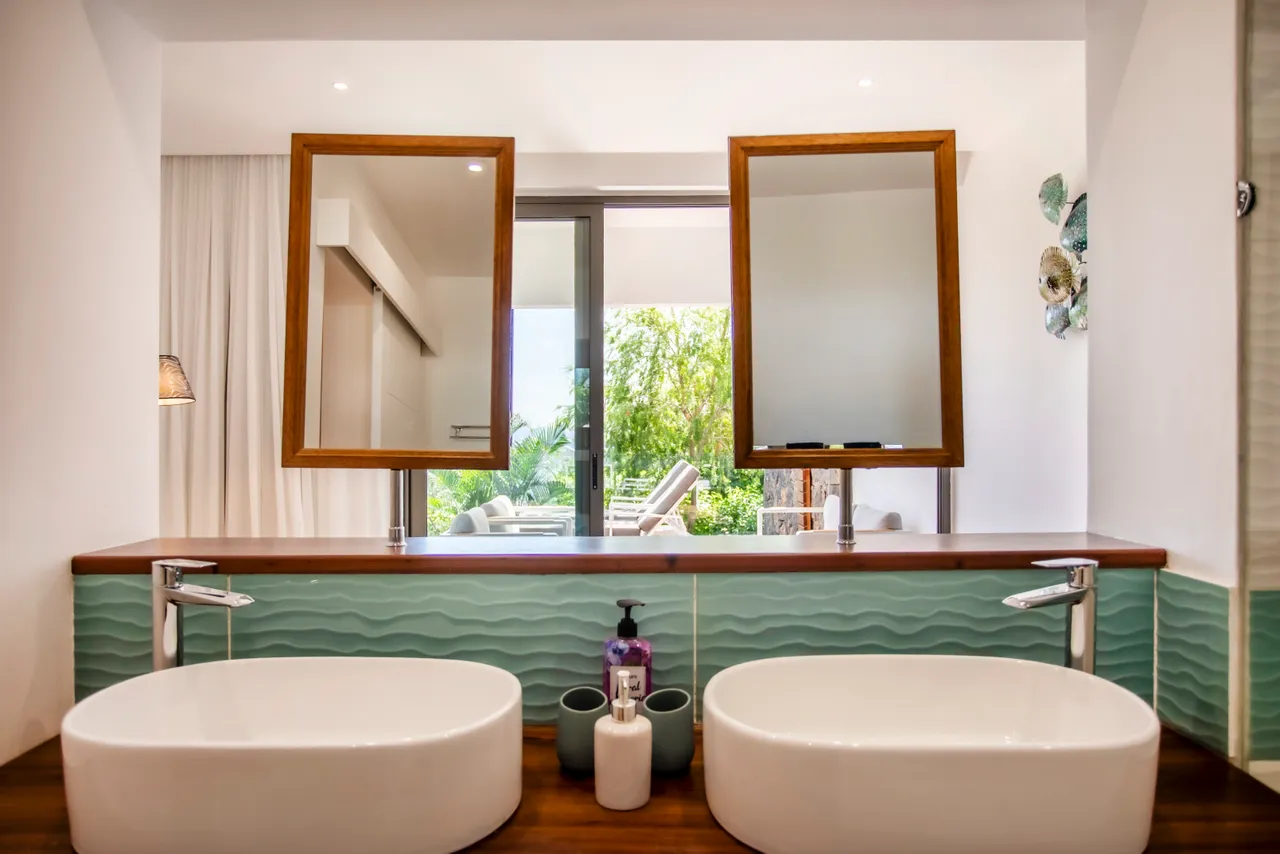 Salle de bain avec double vasque et miroir en bois. Accès à une terrasse verdoyante.