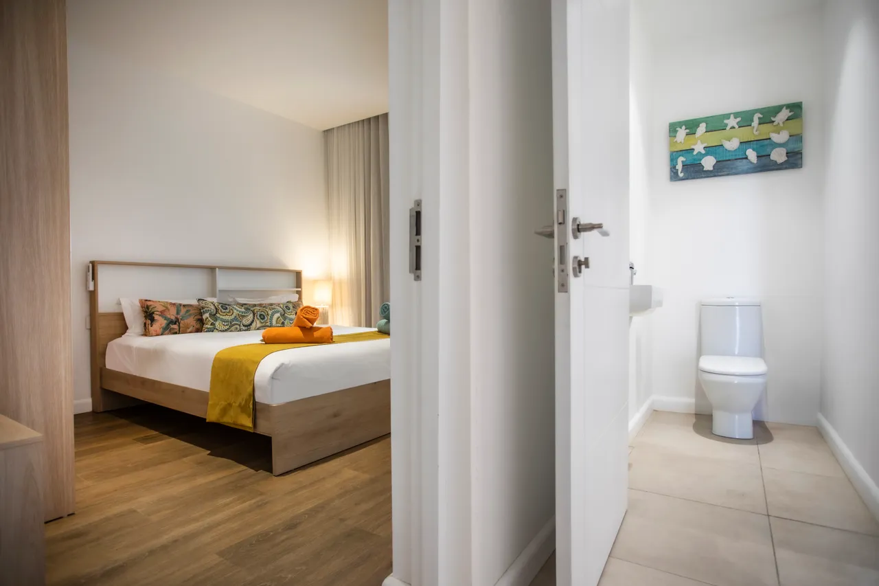 Chambre avec lit double, ornée de coussins colorés. Accès à une salle de bain attenante.
