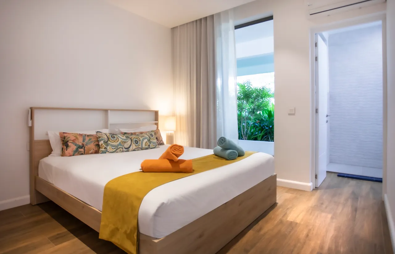 Chambre avec lit double, décorée de coussins et serviettes colorées. Accès à un espace vert.