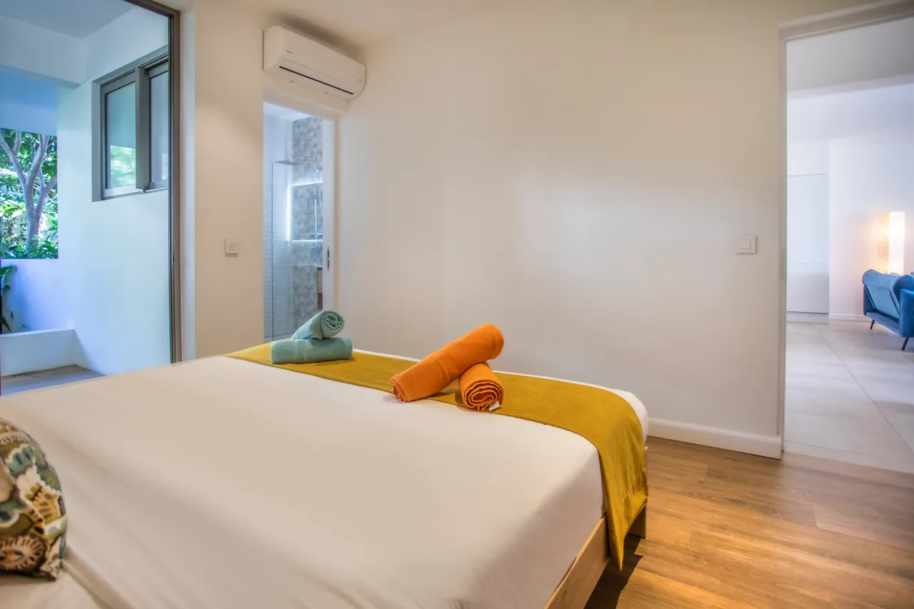Chambre avec parquet en bois et literie blanche. Accès à un espace extérieur.
