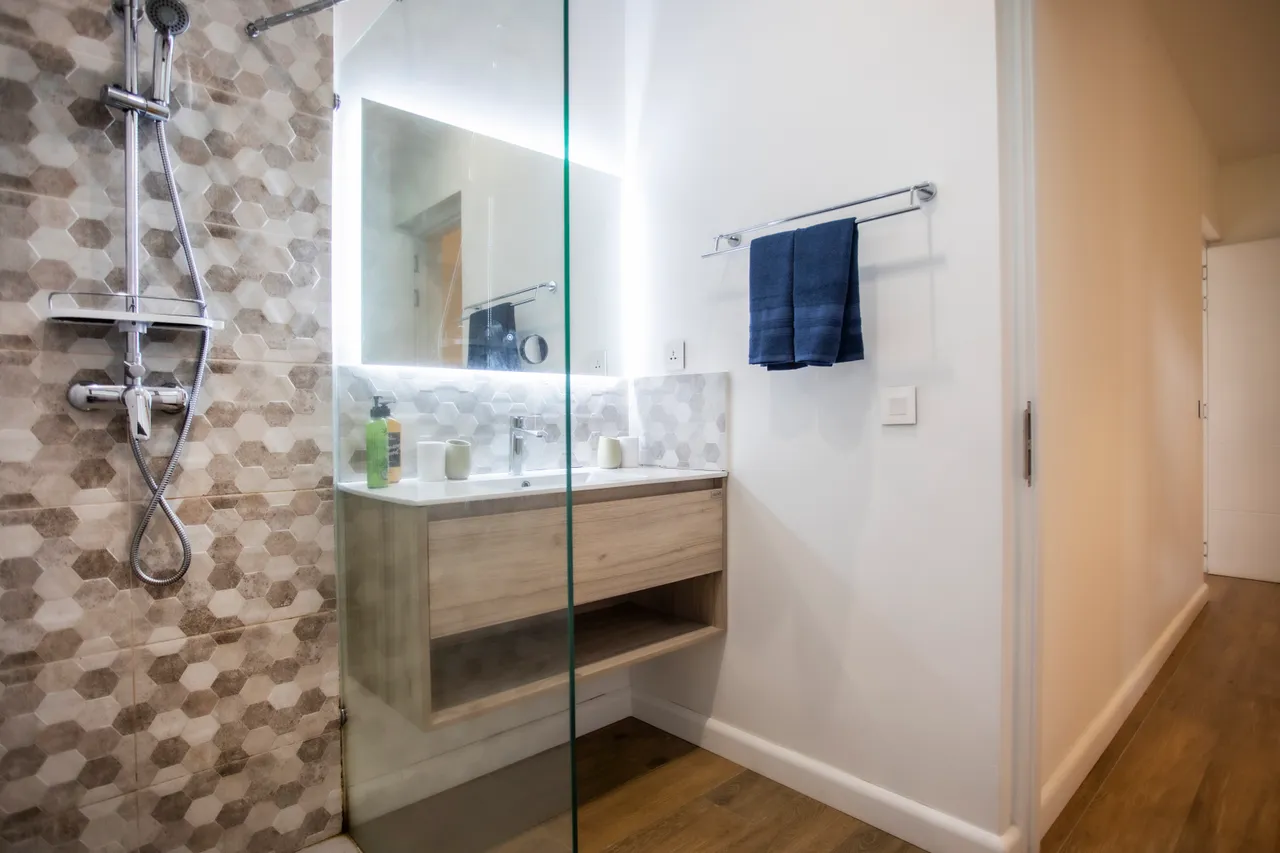 Salle de bain avec douche à l’italienne en verre et meuble sous vasque en bois. Éclairage LED intégré.