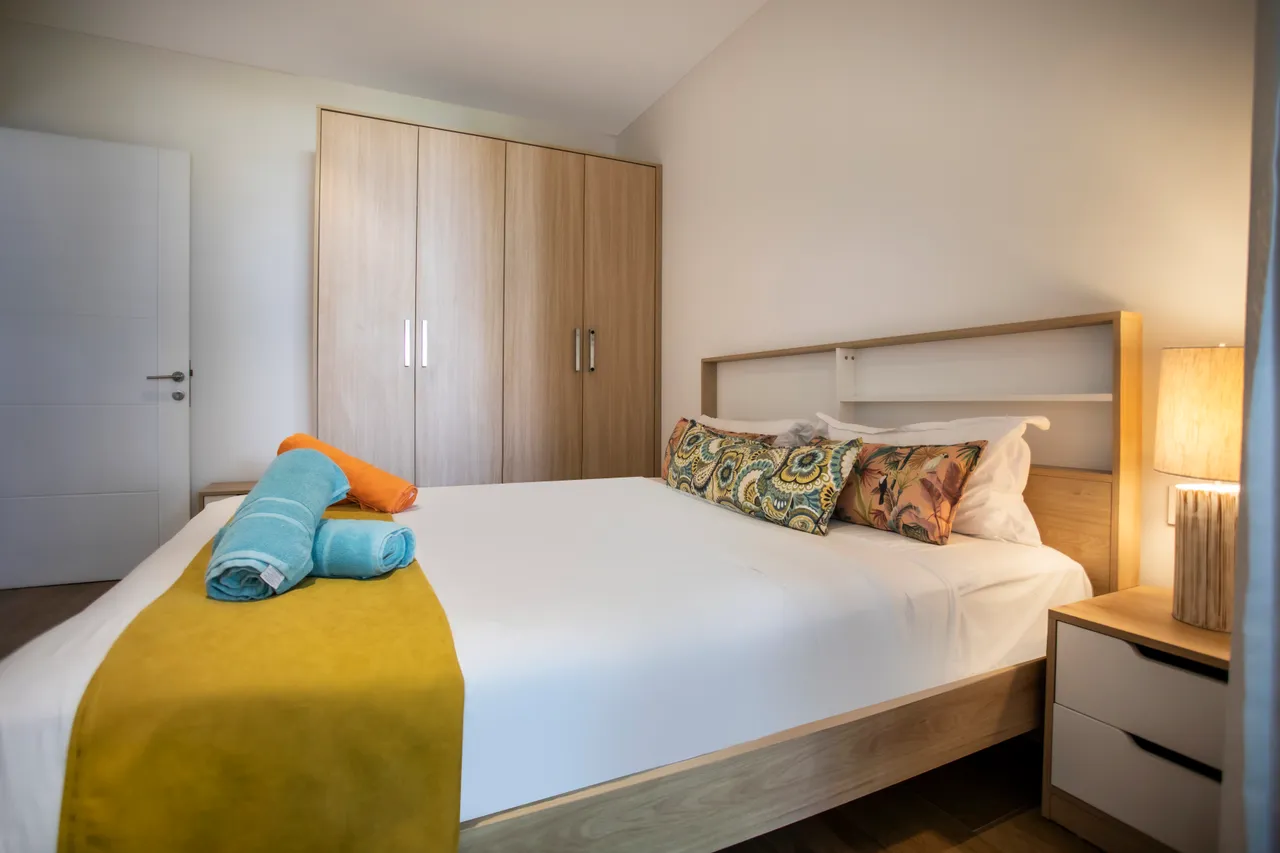 Chambre avec lit double et linge de lit coloré. Rangements intégrés en bois clair.