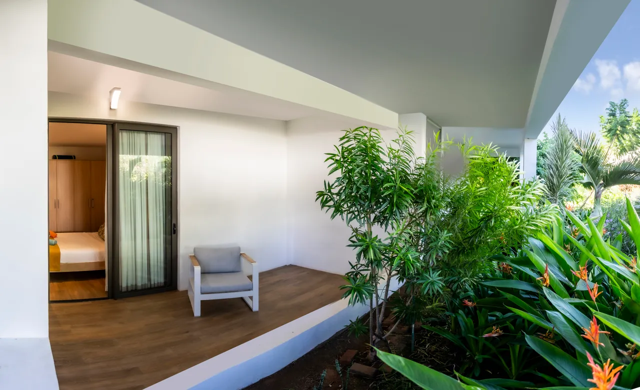 Terrasse avec fauteuil et verdure environnante. Accès à la chambre principale.