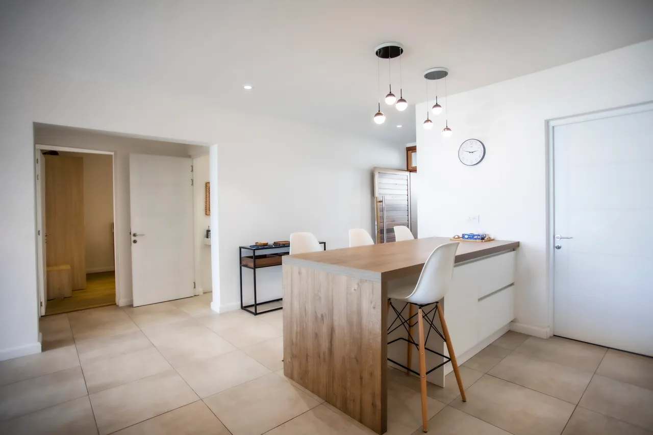 Espace ouvert avec comptoir en bois et tabourets de bar. Lumière naturelle abondante.