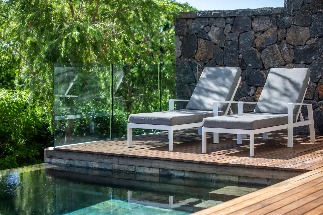 Bois naturel des chaises longues sur la terrasse. Vue sur la piscine et la végétation.