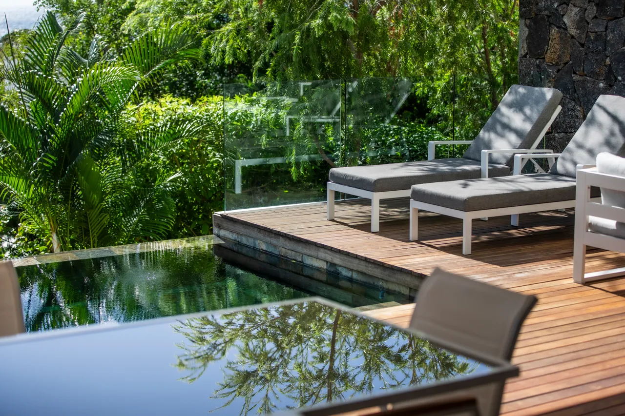 Chaises longues grises sur terrasse en bois, vue sur la piscine.