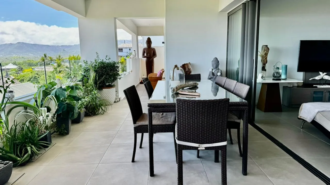 Salle à manger extérieure avec table en verre et chaises en rotin.