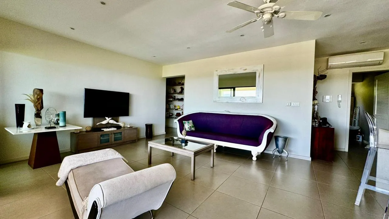 Espace de vie avec un canapé violet et télévision sur mur blanc.