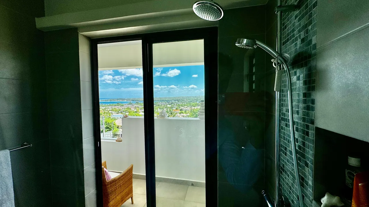 Salle de bain lumineuse avec douche à l'italienne et vue sur la mer.