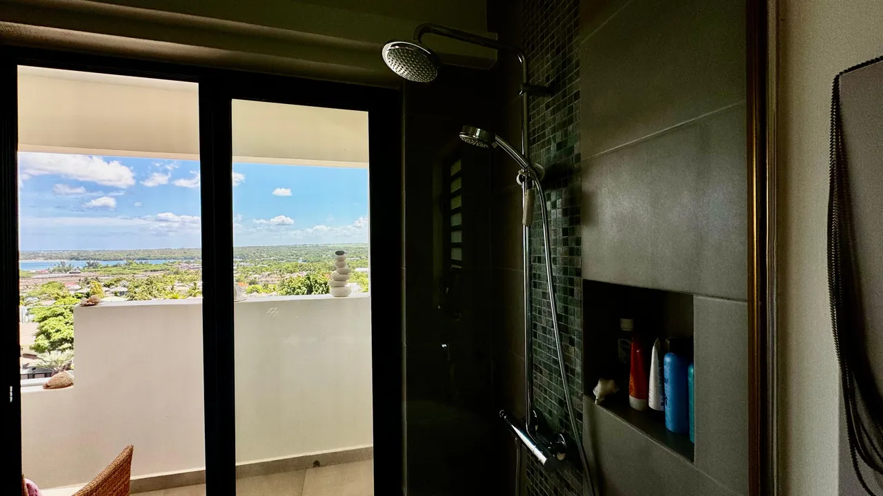 Dalles de carrelage clair dans une salle de bain avec vue sur la mer. Douche à l'italienne et éclairage naturel.