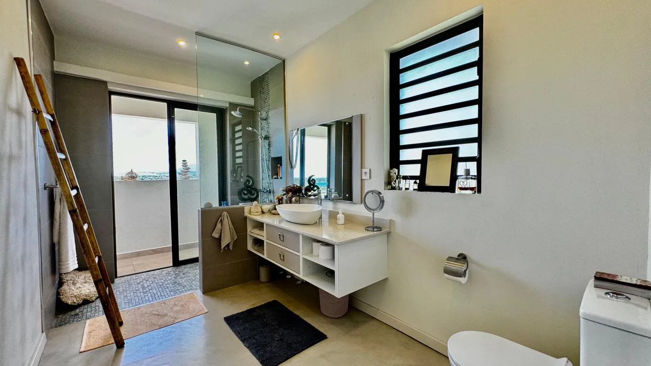 Salle de bain avec grandes fenêtres permettant une vue dégagée sur la mer. Éclairage naturel et espace de rangement.