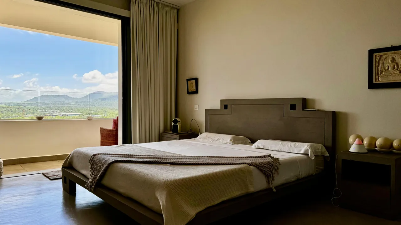 Chambre avec accès à un balcon, offrant une vue panoramique sur l'extérieur. Éclairage naturel par de grandes fenêtres.