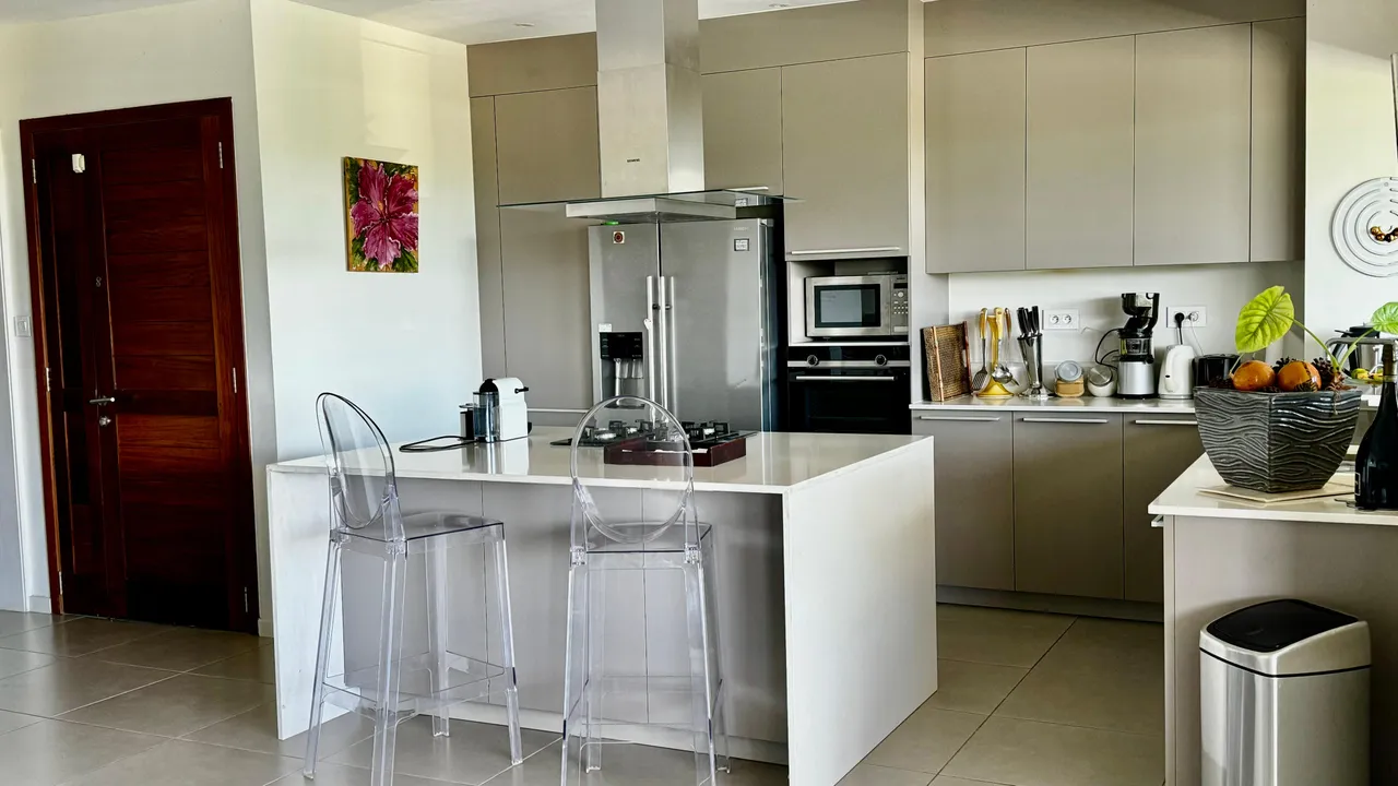 Cuisine moderne avec un bar en quartz et des tabourets transparents. Équipements intégrés et rangements fonctionnels.