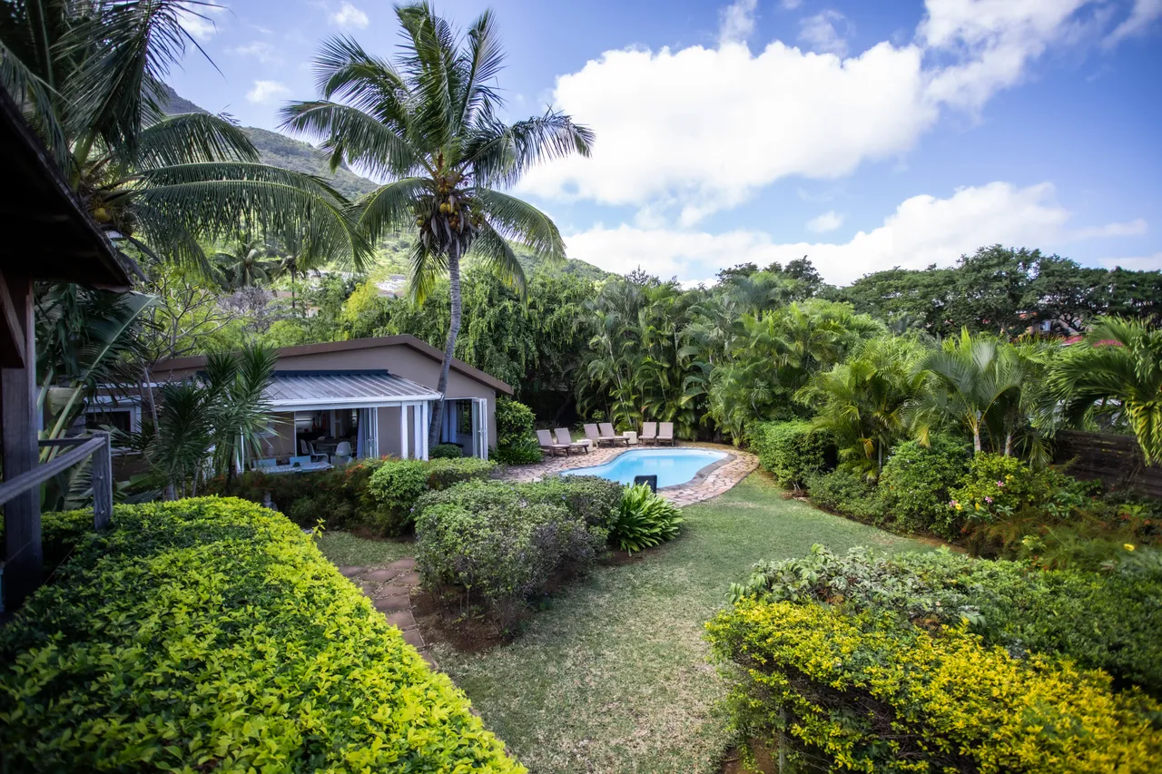 Espace de la galerie offrant une vue dégagée sur le jardin et la piscine.  
Mobilier en rotin dispose d'un coin repas à l'extérieur.  
La disposition permet d'apprécier le cadre verdoyant tout en étant à l'ombre.