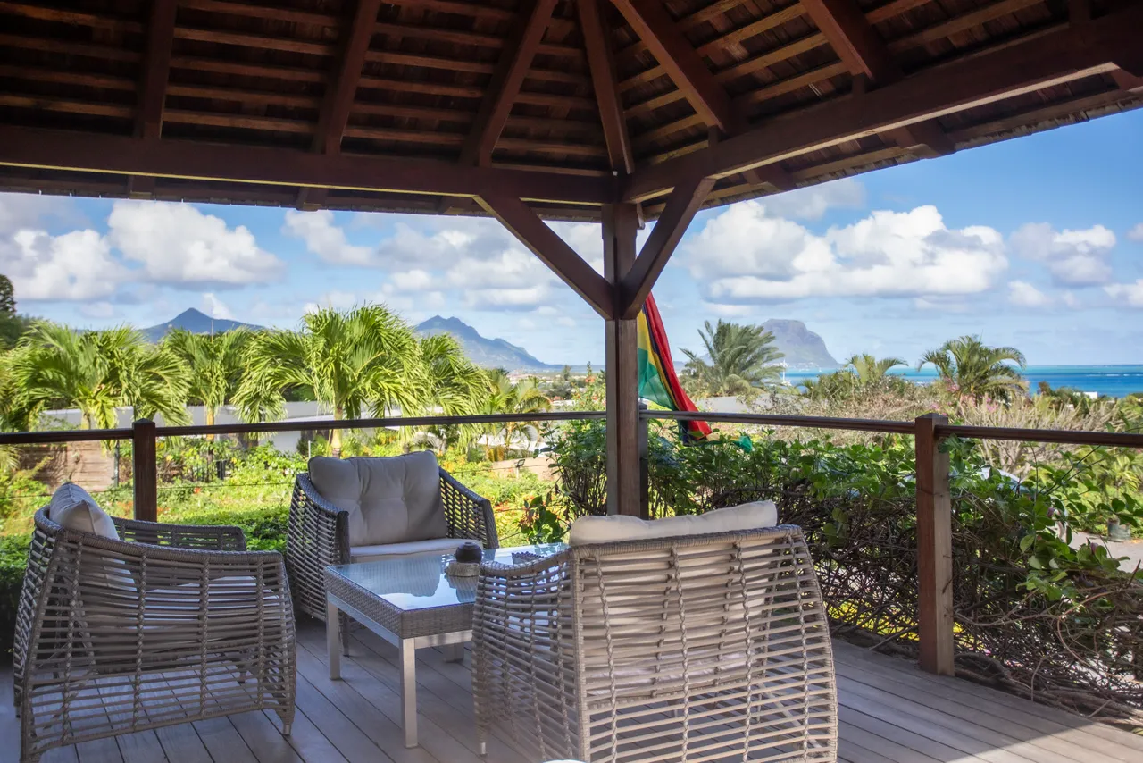Espace de la galerie avec sièges confortables et vue sur la mer.  
Le toit en bois ajoute une touche rustique et esthétique.  
Le mobilier en rotin s'intègre harmonieusement à l'environnement extérieur.  
Ambiance sereine grâce à la proximité de la végétation tropicale.  
Accès direct à la nature environnante depuis cet espace ombragé.  
L'am