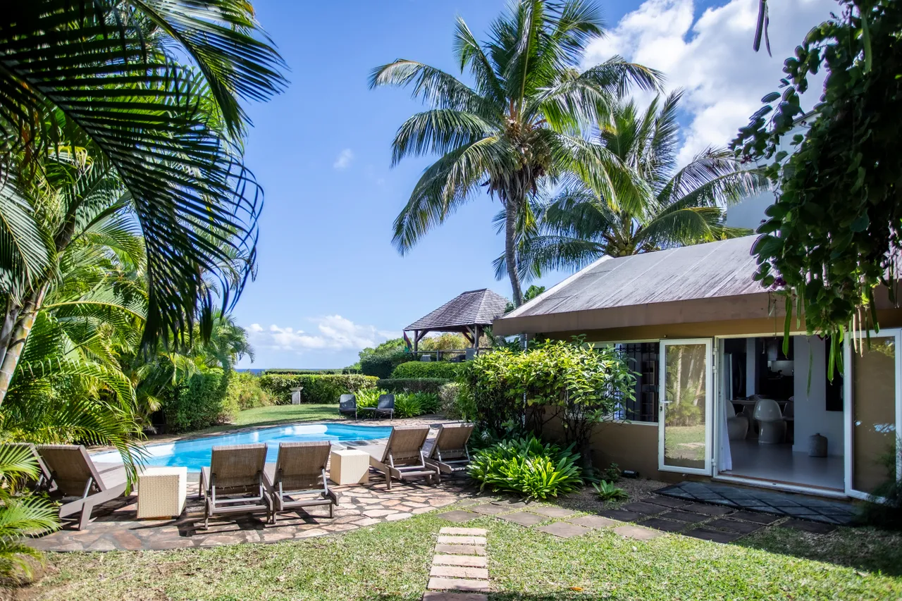Espace extérieur avec chaises longues autour de la piscine.  
Le gazebo en bois offre un coin d'ombre abrité.  
Végétation tropicale encadre l'espace, créant une atmosphère sereine.  
Vue sur la mer depuis la piscine, apportant fraîcheur et lumière.  
La disposition des chaises permet de profiter du soleil.