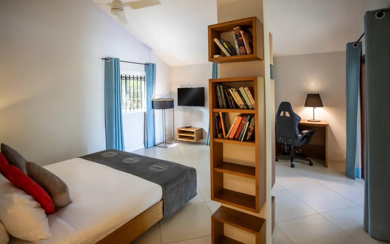Couleurs neutres instaurent une ambiance apaisante dans la chambre.  
Étagères en bois intégrées offrent un espace de rangement fonctionnel.  
Fenêtres avec rideaux légers laissent filtrer la lumière naturelle.  
Coin bureau équipé d'une chaise ergonomique pour un espace de travail.  
Luminaires modernes apportent un éclairage doux et agréable à l'ensemble.