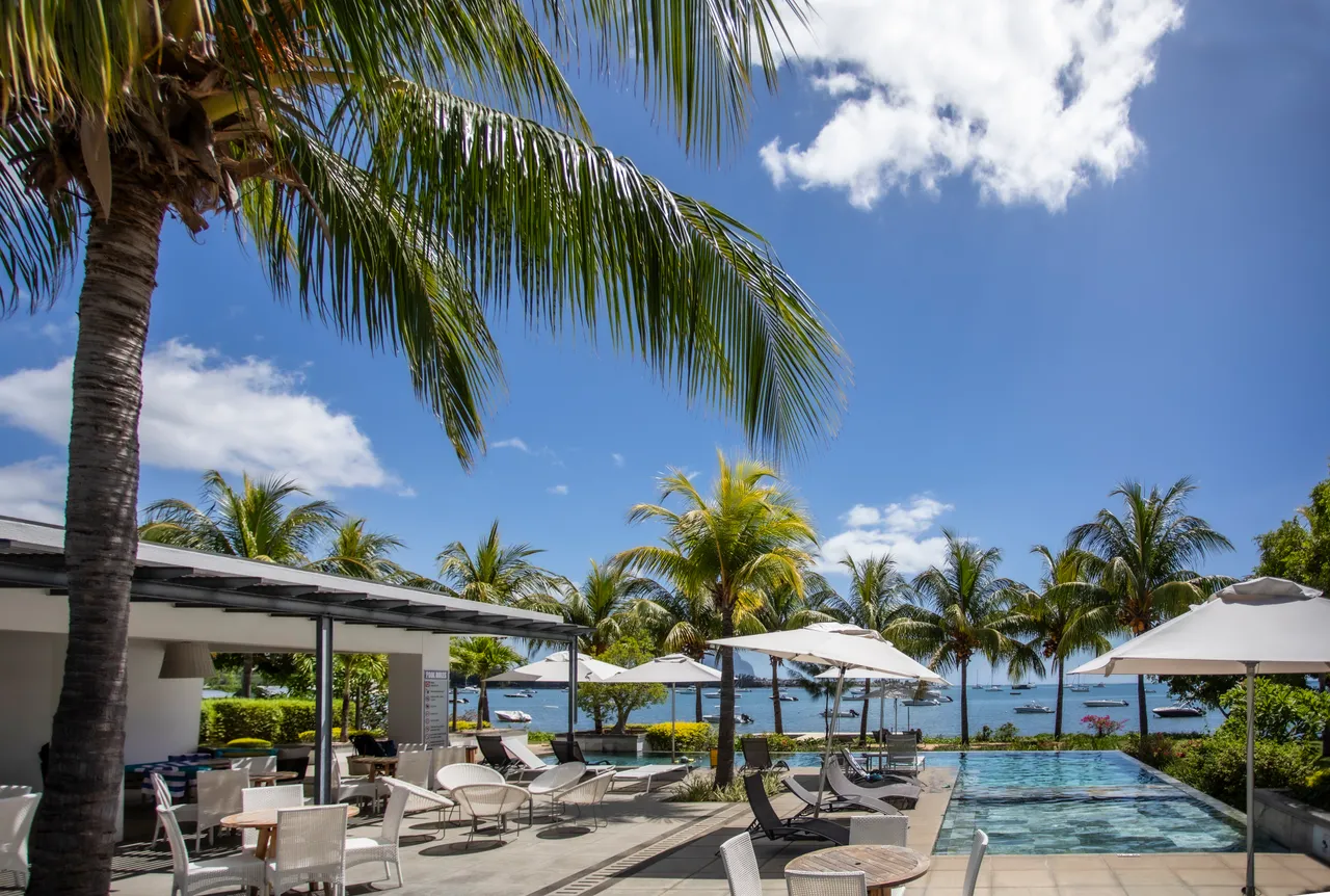 La piscine longe la terrasse, avec des transats et des parasols face à la mer.