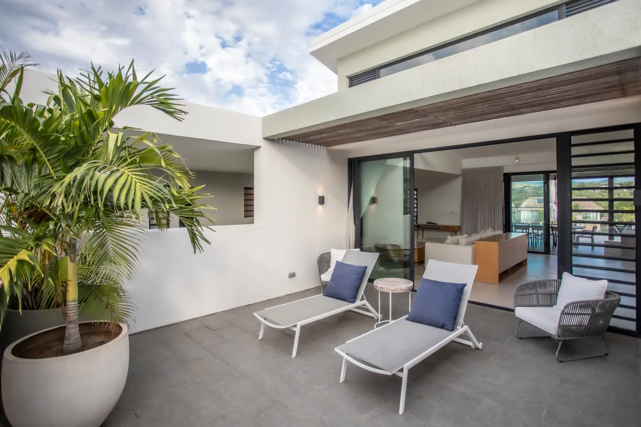 Terrasse en dalles grises équipée de chaises longues. Plantes tropicales ajoutent une touche verte au décor. Espace extérieur agrémenté d'un mobilier contemporain en tissu. Vue dégagée sur la nature environnante depuis la terrasse. Coin détente lumineux et ouvert sur l'extérieur.