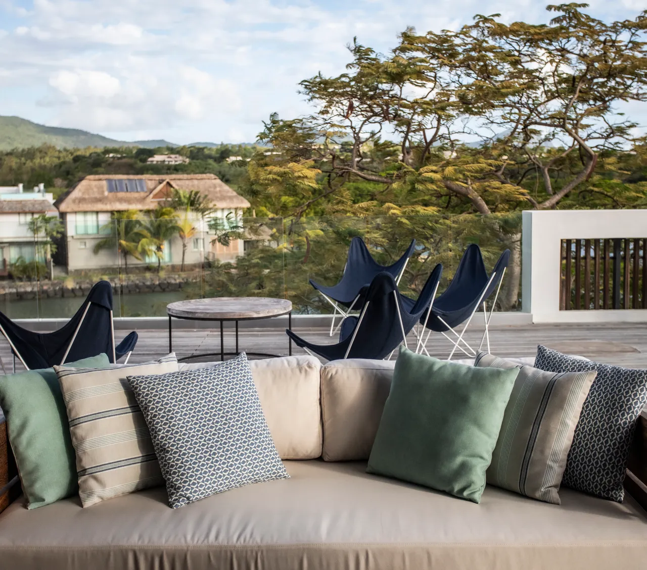 Tons neutres et texture douce des coussins sur le canapé extérieur. Vue dégagée sur la nature environnante depuis l'espace détente. Mobilier en tissu clair offrant un confort pour se relaxer. Coin repas en plein air avec accès facile à l'intérieur. Plantes vertes ajoutant une touche de fraîcheur à l'ensemble.