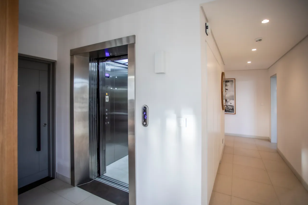 Ascenseur moderne facilitant l'accès à tous les niveaux du penthouse.  
Mur en blanc sobre et carrelage clair ajoutent une touche contemporaine.  
Éclairage intégré offrant une luminosité uniforme dans la galerie.  
Espace dégagé permettant une circulation aisée entre les pièces.  
Détails architecturaux subtils soulignant le design fonctionnel de l'entrée.