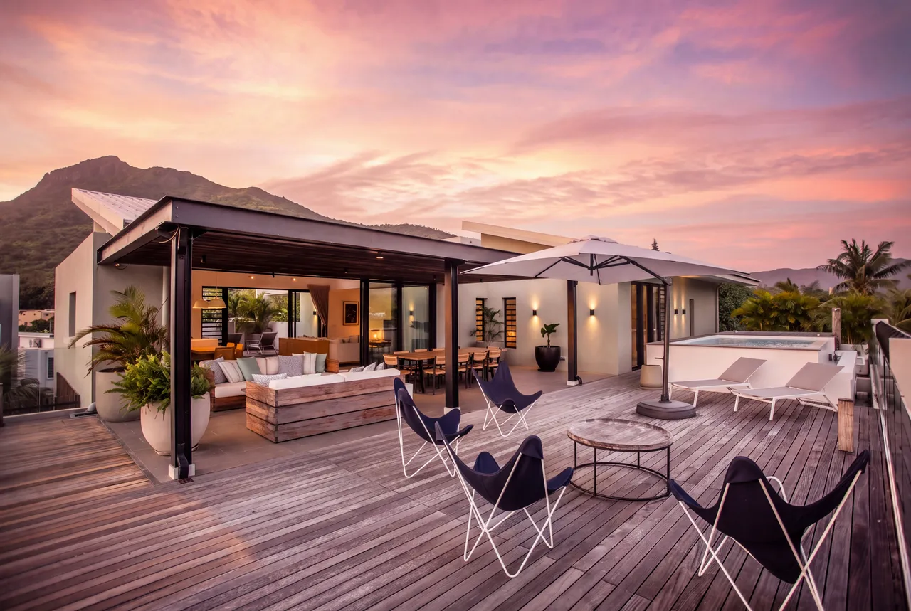 Bois gris dominant, la terrasse réunit fauteuils pliants, canapé et piscine sous un ciel rosé.