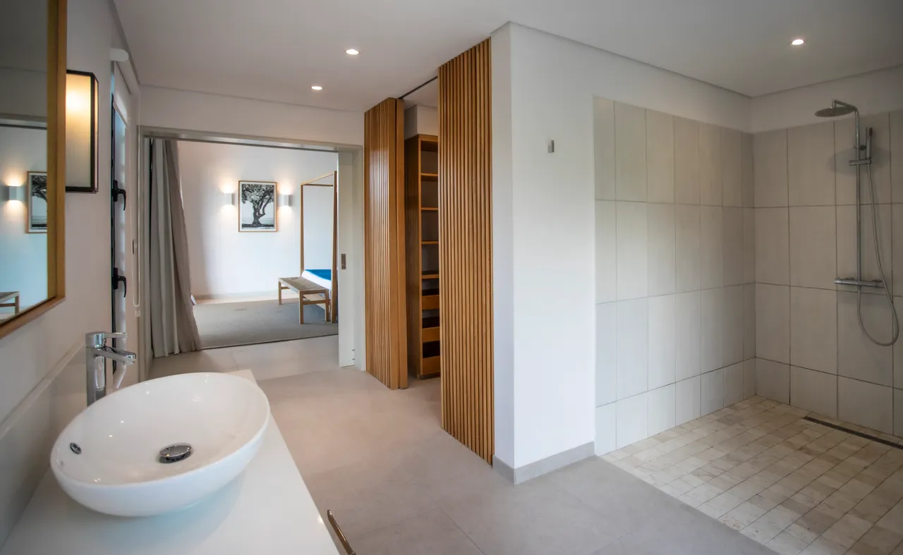 Salle de bain équipée d'une grande douche à l'italienne et de carrelage clair. 

Miroir encadré ajoutant une touche moderne à l'espace. 

Rangement intégré en bois maximisant l'efficacité du lieu. 

Fenêtre ouvrante apportant lumière naturelle et vue sur l'extérieur. 

Éclairage intégré créant une ambiance douce et contemporaine.