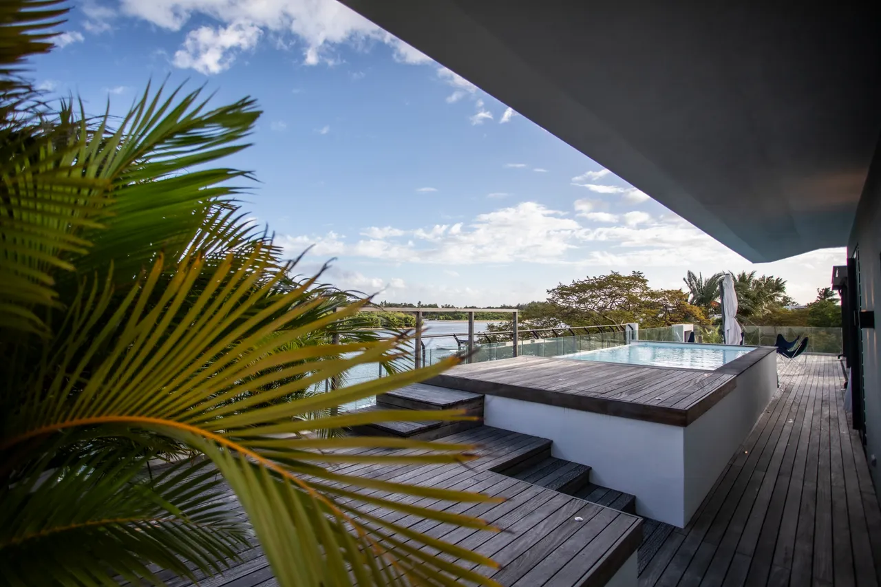 Galerie offrant un accès direct à la piscine et à la terrasse. 

Vitrages larges maximisant la lumière naturelle dans l'espace. 

Plantes vertes ajoutant une touche de nature à l'environnement. 

Terrasse en bois permettant de profiter du cadre extérieur. 

Espace ouvert favorisant la circulation et le confort.