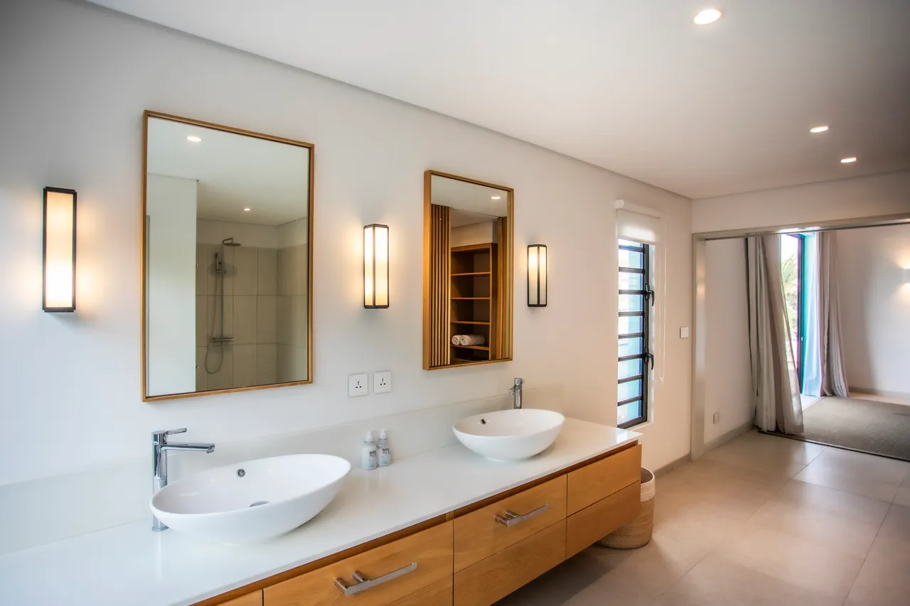 Salle de bain avec double vasque et grands miroirs. 

Rangement intégré en bois offrant fonctionnalité et esthétique. 

Douche à l'italienne avec carrelage clair pour un design minimaliste. 

Fenêtre laissant entrer la lumière naturelle et offrant une vue. 

Éclairage moderne ajoutant une ambiance agréable à l'espace.