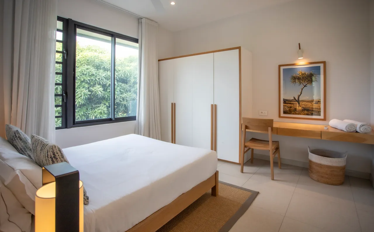 Chambre lumineuse avec fenêtre offrant une vue sur la végétation. 

Mobilier en bois incluant un bureau et une chaise. 

Tons clairs des murs créant une atmosphère sereine. 

Espace de rangement intégré optimisant l'utilisation de la pièce. 

Linge de lit et serviettes soigneusement disposés sur le mobilier.