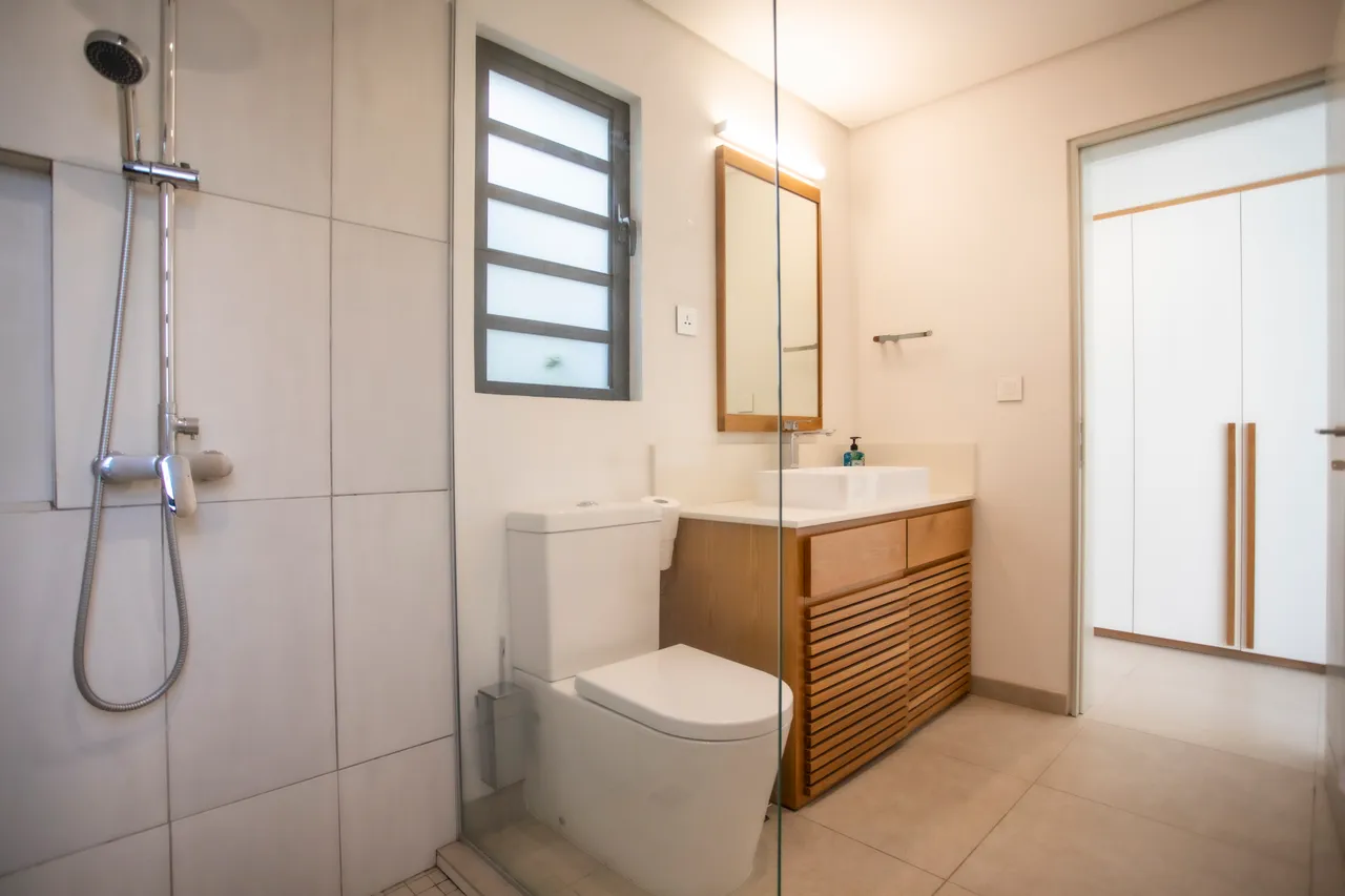 Salle de bain avec douche séparée et carrelage clair. 

Rangement en bois intégrant une vasque moderne. 

Éclairage encastré créant une ambiance douce et chaleureuse. 

Fenêtre apportant lumière naturelle et ventilation. 

Miroir au-dessus de la vasque ajoutant de la fonctionnalité.