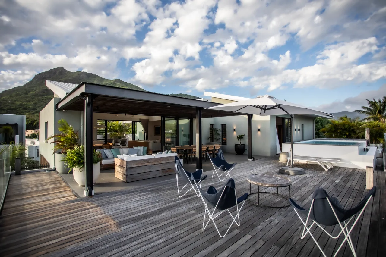 Galerie extérieure avec espace de vie confortable et vue sur la montagne. 

Mobilier en bois et sièges en toile favorisant une ambiance détendue. 

Parasols offrant de l'ombre pour se protéger du soleil. 

Terrasse en bois ajoutant un aspect chaleureux à l'environnement. 

Piscine privée visible, intégrant harmonieusement l'espace extérieur.
