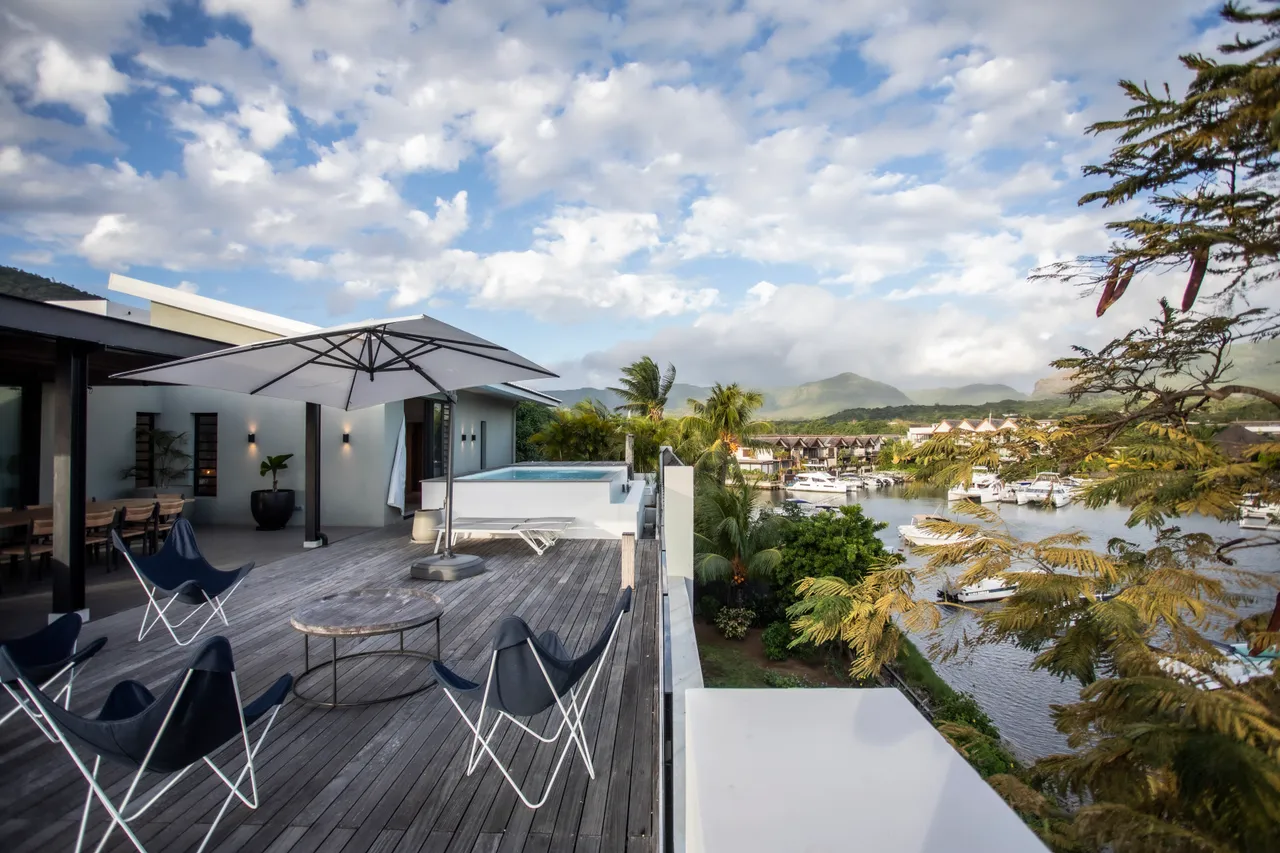 Terrasse en bois avec vue sur le port et les montagnes. 

Mobilier d'extérieur moderne offrant des sièges confortables. 

Parasols fournissant de l'ombre pour des moments de détente. 

Espace propice à la convivialité pour des repas en plein air. 

Zone de relaxation intégrant des chaises longues près de la piscine.