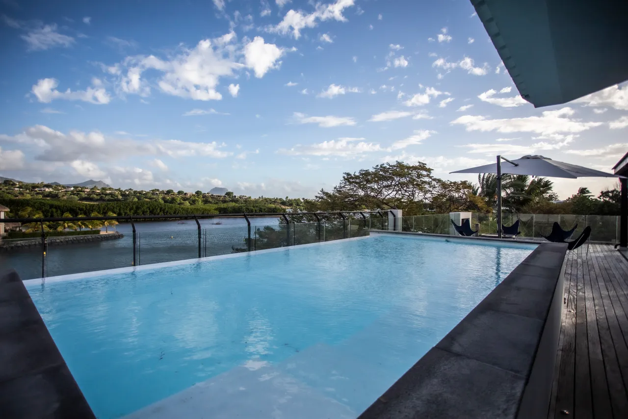Terrasse avec piscine à débordement offrant une vue panoramique sur l'eau. 

Mobilier en bois disposé pour des moments de détente en extérieur. 

Parasols positionnés pour assurer de l'ombre au bord de la piscine. 

Espace de vie extérieur intégrant des chaises longues pour se relaxer. 

Éclairage extérieur créant une atmosphère agréable lors des soirées.