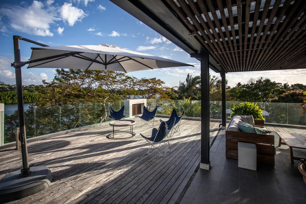 Terrasse en bois avec mobilier confortable pour des moments de détente. 

Parasol offrant de l'ombre sur la zone de vie extérieure. 

Vue dégagée sur la nature environnante ajoutant une dimension apaisante. 

Espace de vie extérieur intégré favorisant des moments conviviaux. 

Chaises longues positionnées pour profiter du soleil près de la piscine.