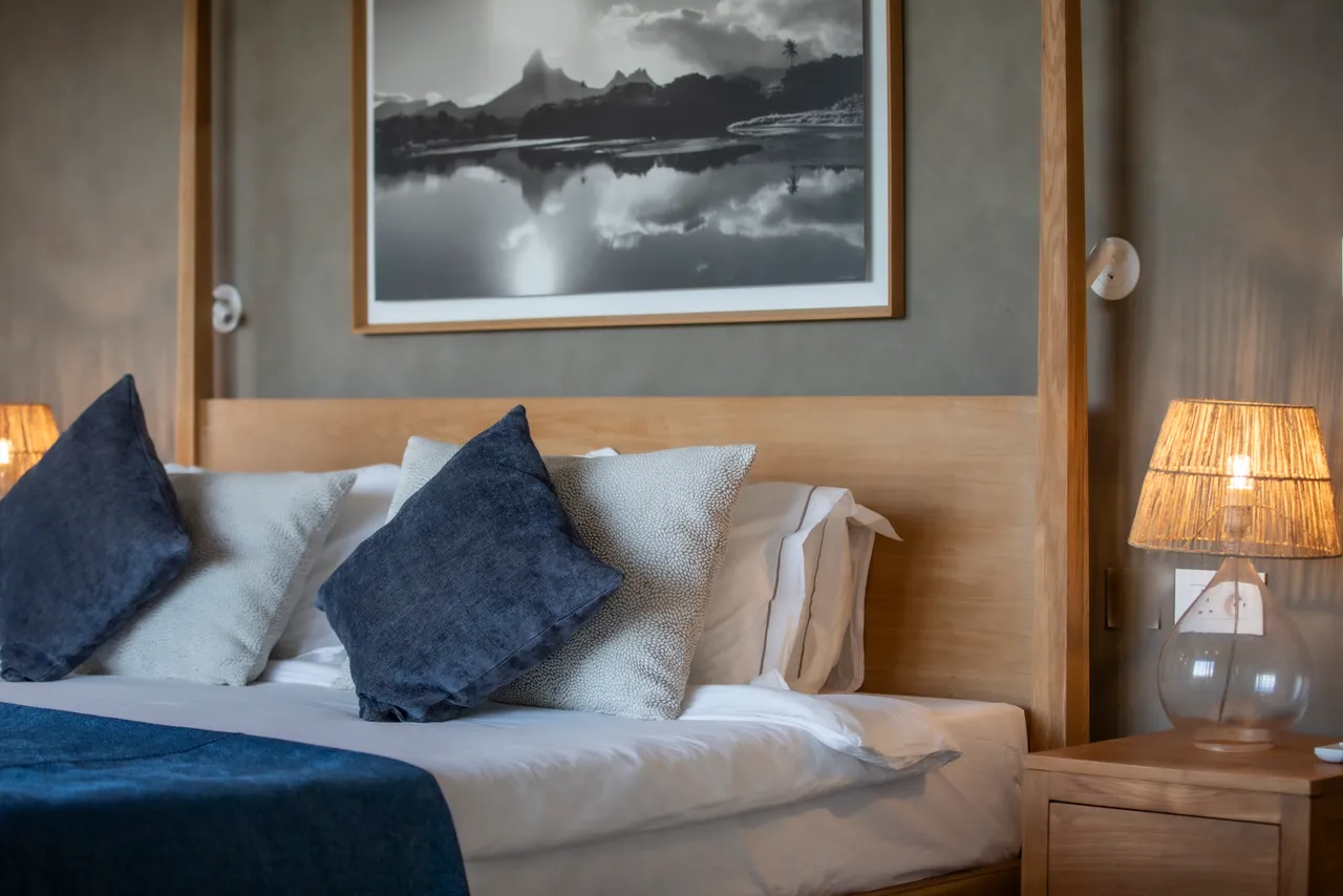 Chambre avec un lit double et décoration sobre en ton neutre. 

Éclairage doux provenant des lampes de chevet disposées de chaque côté. 

Oeuvre d'art en noir et blanc apportant une touche esthétique à l'espace. 

Fenêtres offrant une vue sur la nature environnante pour une ambiance calme. 

Mobilier en bois créant une atmosphère chaleureuse et ap