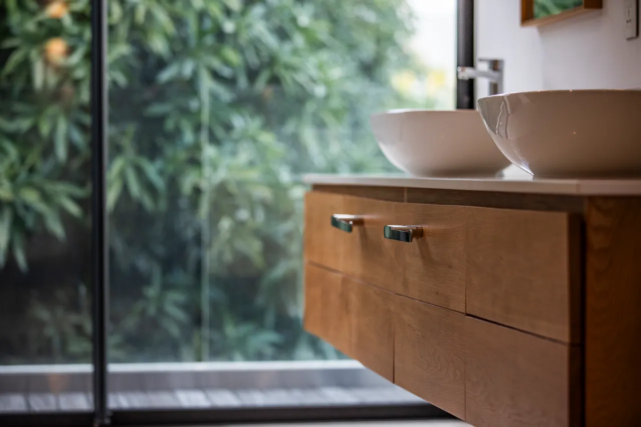 Salle de bain moderne avec double vasque en céramique sur meuble en bois. 

Grandes fenêtres permettant d'apprécier la verdure extérieure tout en s'isolant.