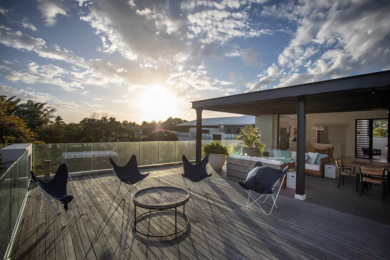 Espace extérieur avec chaises longues pour profiter du coucher de soleil. 

Terrasse en bois dotée d'un coin salon pour des moments de détente. 

Vue dégagée sur le ciel et la végétation environnante depuis la terrasse. 

Zone de repas extérieure équipée d'une table pour des repas conviviaux. 

Parasol sur la terrasse offrant un ombrage pour se protéger du soleil