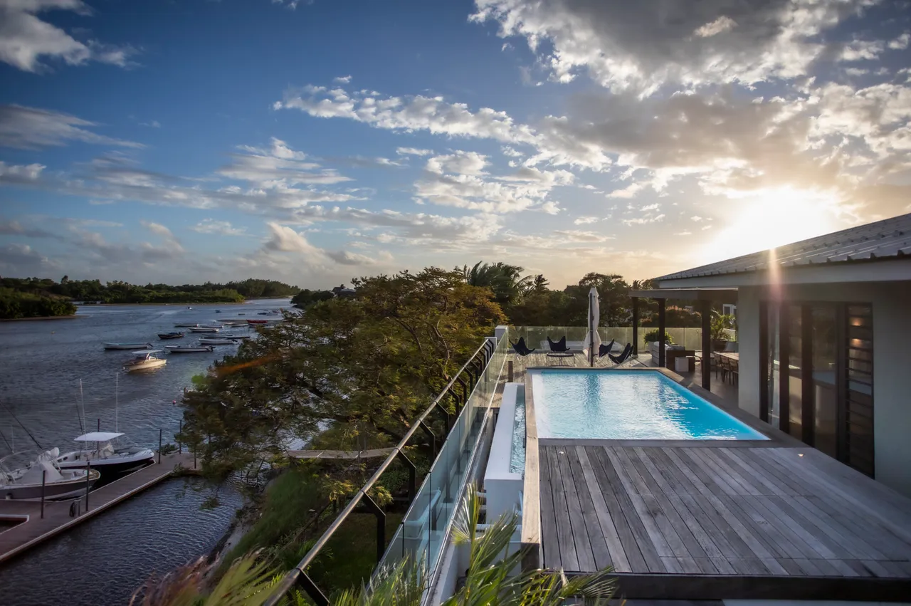 Terrasse surplombant le port avec piscine privée pour baignade. 

Vue dégagée sur la rivière et les bateaux amarrés. 

Mobilier extérieur en bois pour des moments de détente au soleil. 

Végétation environnante offrant une intimité à l'espace extérieur. 

Espace de vie lumineux avec accès direct à la terrasse.
